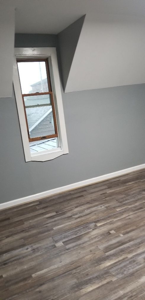 Bedroom interior with a window in a sloped wall, gray walls, and wood-look flooring.