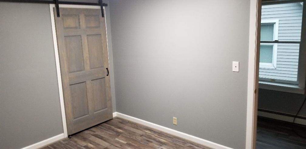 A room with a gray wall, a barn door, and a window on the right.