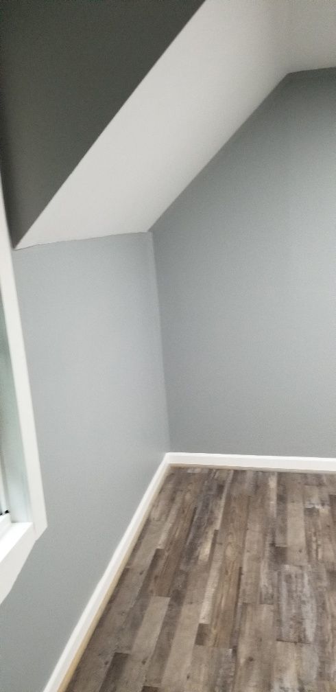 An empty room with gray walls and wood-look flooring. White trim accents the base and ceiling.