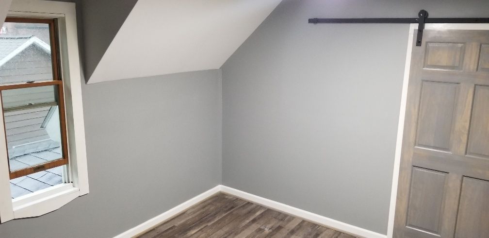 A room with gray walls and a barn door, a window, and wood-look flooring.