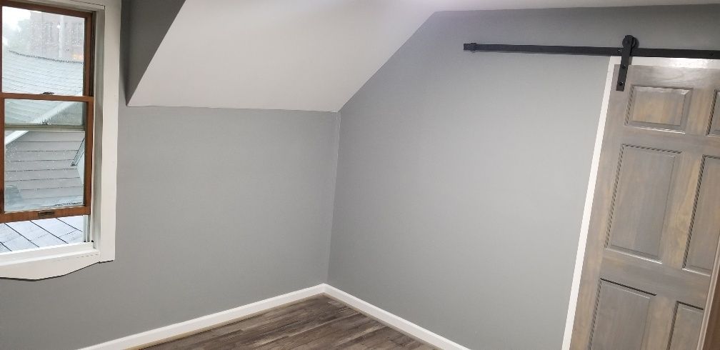 An empty room with gray walls, a window, a sliding door, and a white angled ceiling.