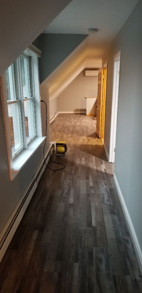 Interior hallway with wood-look flooring and a sloped ceiling leading to a room.