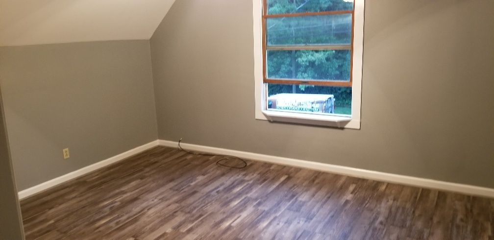 Empty room with gray walls, wood-look flooring, and a window overlooking greenery.