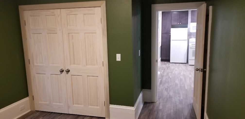 Closet doors and a doorway to a kitchen, green walls, light wood-look floor, and white trim.