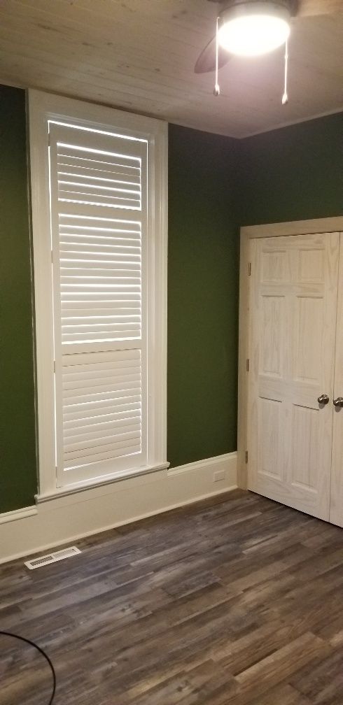 Room with green walls, white shutters, and a wooden floor. A closed white door is on the right.