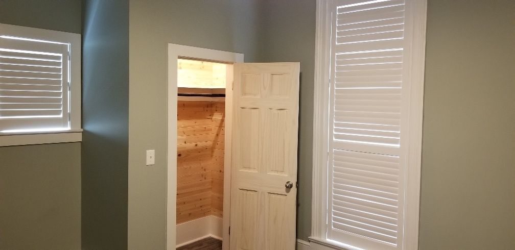 A closet door open inside a room with a window and shutters. The walls are gray.