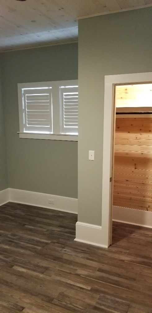 Interior of a room with sage green walls, white trim, wood flooring, and a doorway to a wood-paneled closet.