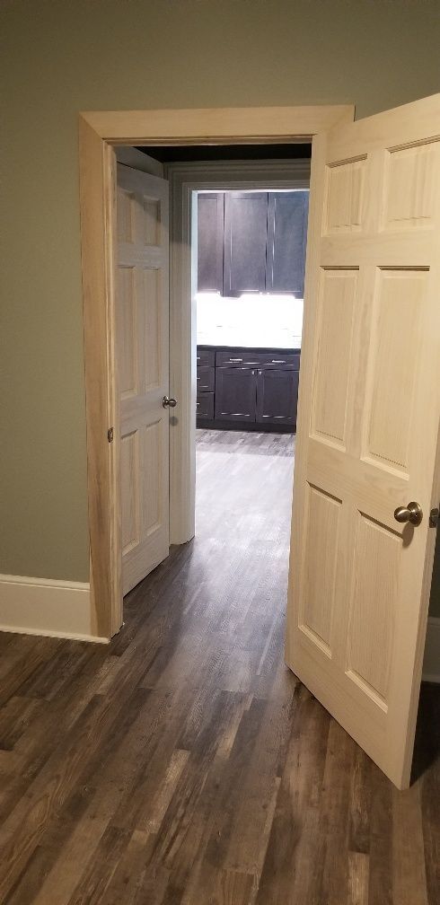 Open doorway to a kitchen with dark cabinets. White doors with detailed trim. Gray-brown wood floor.