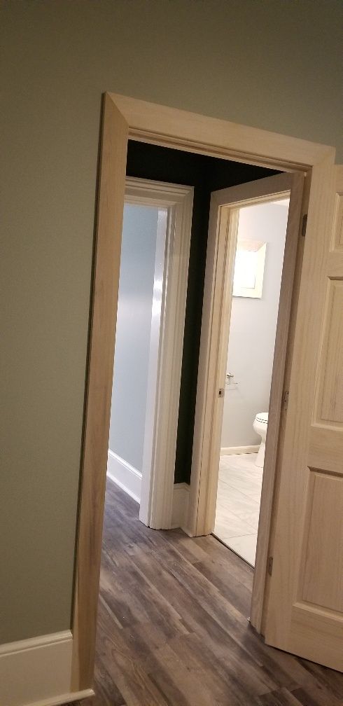 View into a hallway with several doorways. One leads to a bathroom with a toilet. Light wood trim on door frames.