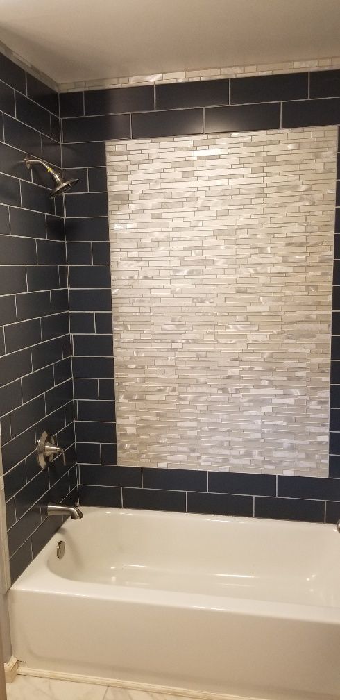 A white bathtub with dark blue tiled walls and a light-colored mosaic tiled accent.