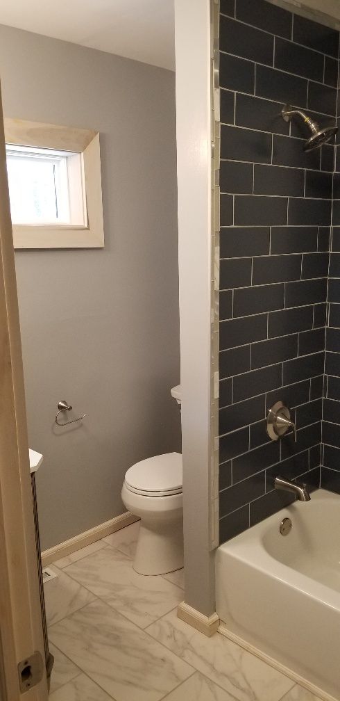 Bathroom with gray walls, white toilet, dark tile shower, and a small window.