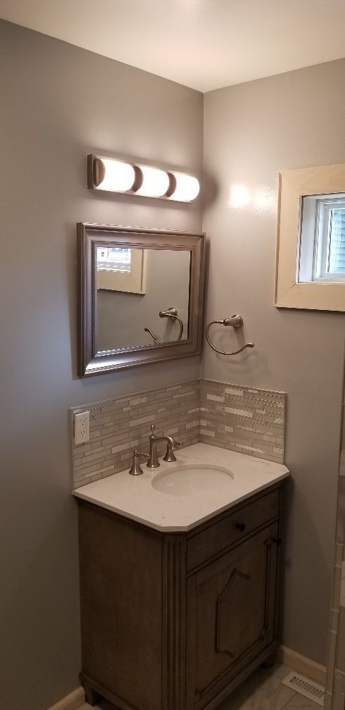 Bathroom vanity with mirror, lighting, and sink on a gray wall.