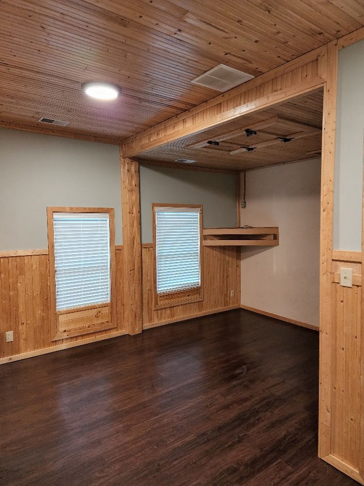Empty room with wood paneling, wood floor, and two windows with blinds.