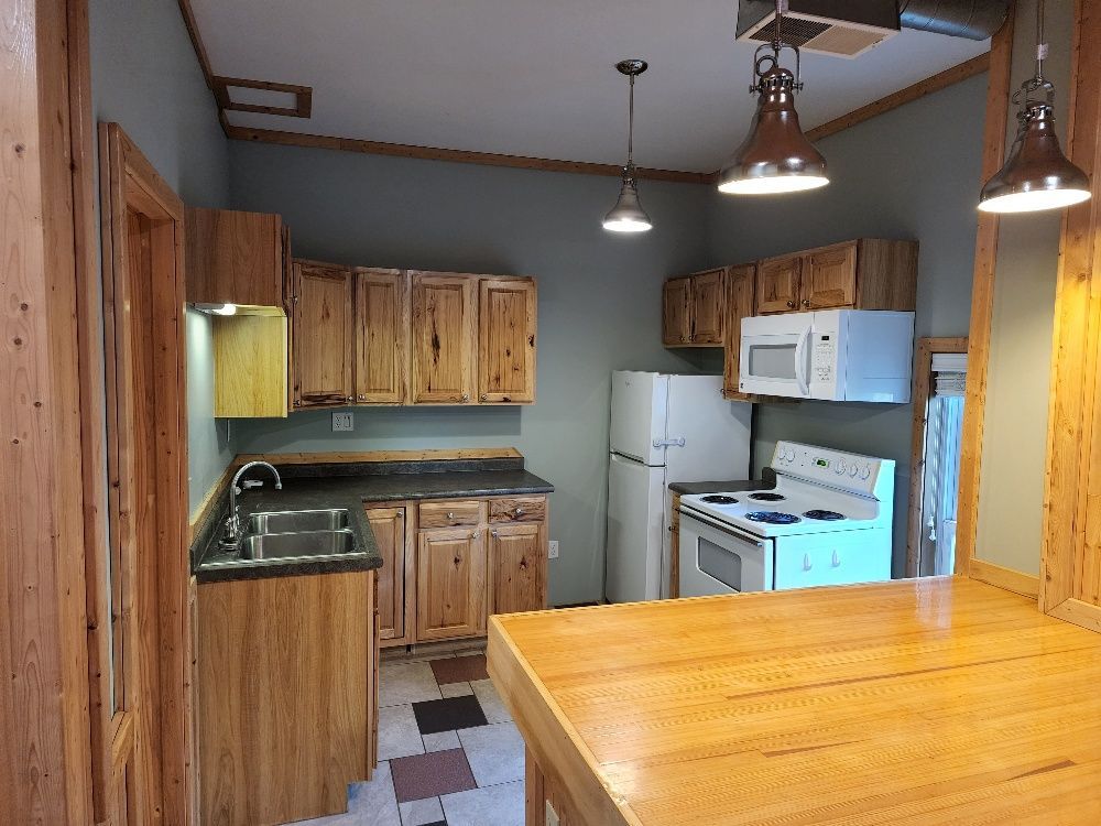 Kitchen with light wood cabinets, gray walls, white appliances, and a butcher block island.