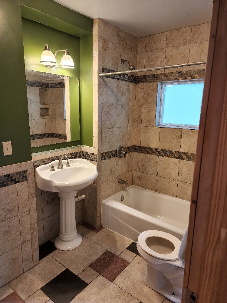 Bathroom with pedestal sink, toilet, tub/shower, tiled walls, and green accent walls.