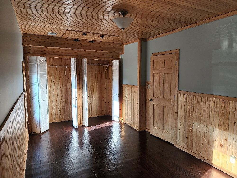 Wooden-paneled bedroom with closet, door, dark wood floor, and patterned ceiling.