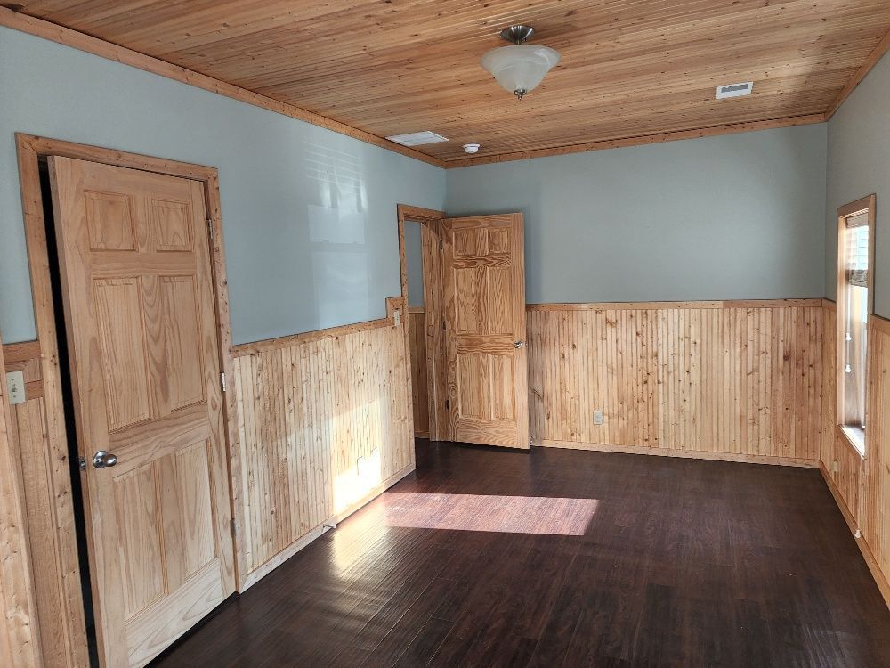 Empty room with wood paneling, wood doors, wood ceiling, dark floor, and light blue walls.