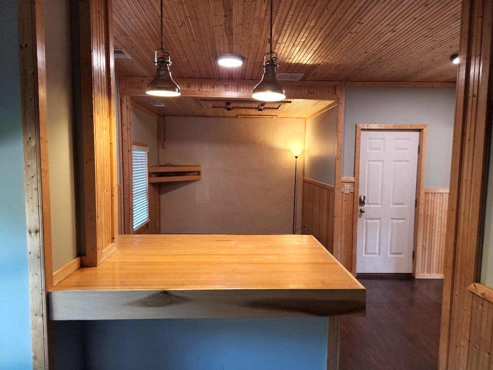 Interior with wood paneling, a bar, and two pendant lights. A white door is visible.