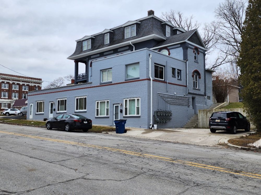 Two-story blue building with a black car parked in front, on a gray day.