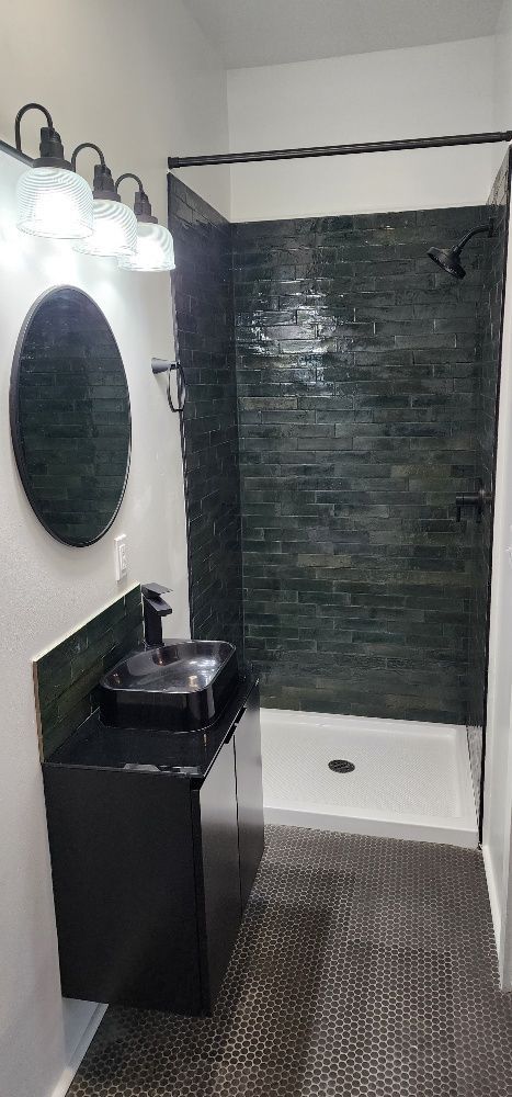 Bathroom with black vanity, dark green shower tile, and oval mirror.