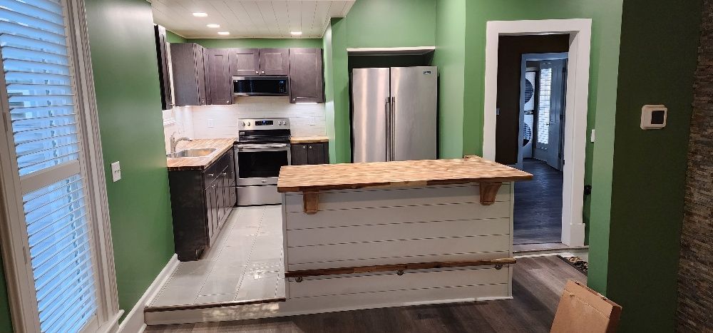 Kitchen renovation with dark brown cabinets, stainless steel appliances, and green walls. A new island is under construction.