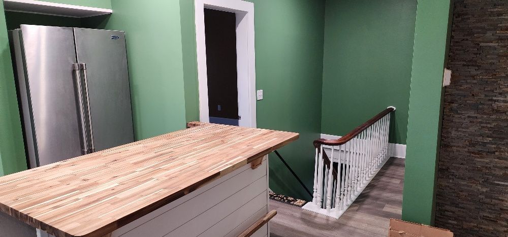 A kitchen with a stainless steel refrigerator, wooden countertop, and staircase leading up. The walls are green.