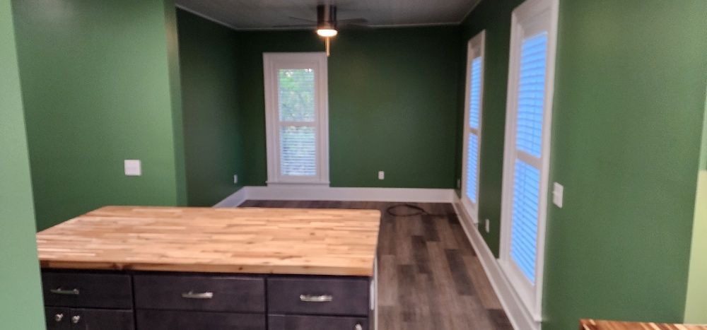 Interior kitchen with green walls, a wooden countertop, and dark cabinets. There are windows.
