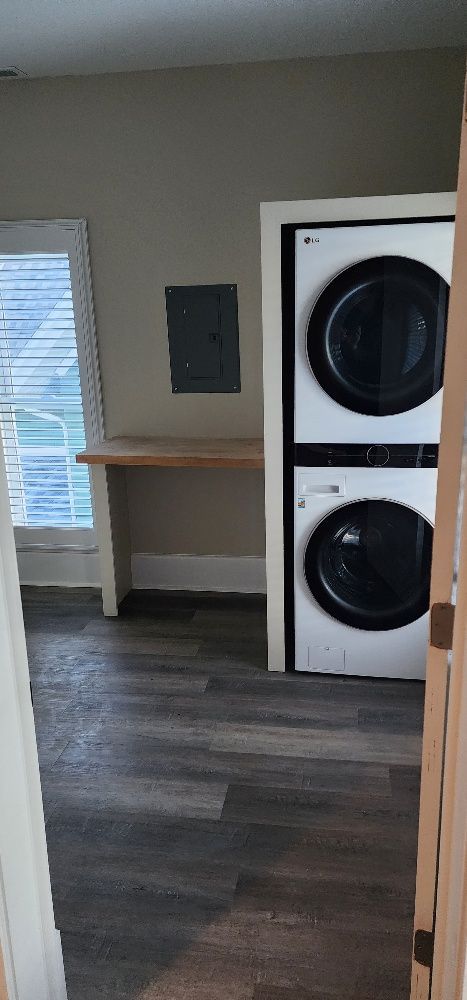 A laundry room with a stacked washer and dryer, a wooden desk, and a window.