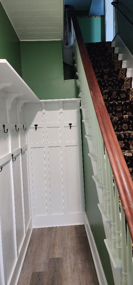 Stairwell with white wainscoting and coat rack, green walls, and wood-paneled floor.