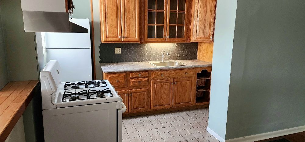 A kitchen with light wood cabinets, a white stove, and a refrigerator.
