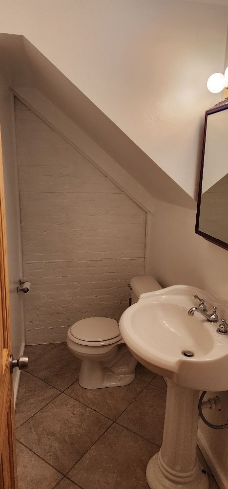 A small bathroom with a toilet, sink, and mirror. The angled ceiling is white.
