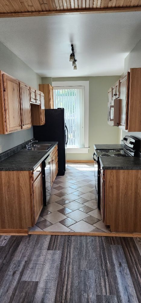 Kitchen with wooden cabinets, dark countertops, and tile and laminate flooring.  A window is in the back.