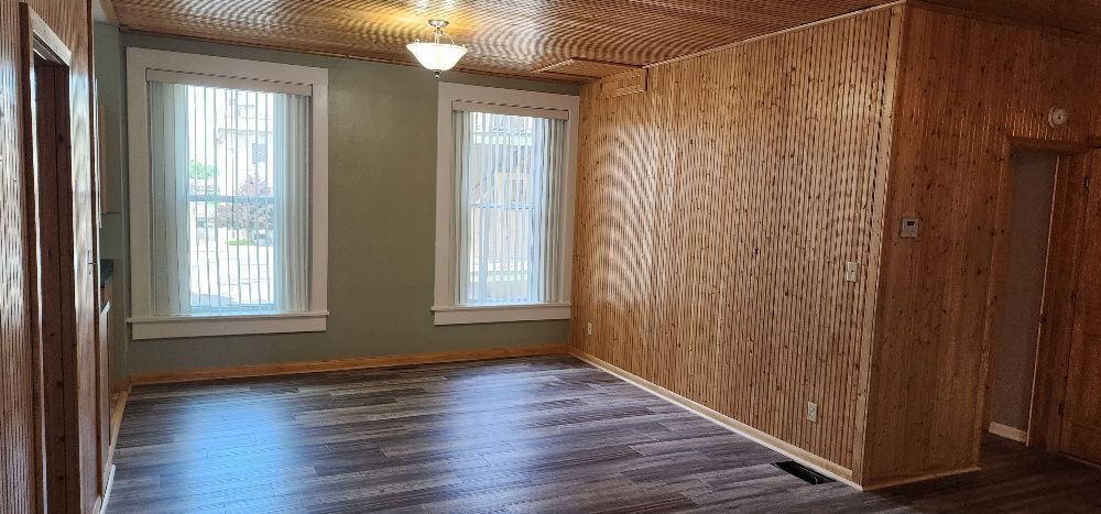 Interior of a room with wood paneling on the walls and ceiling, two windows, and dark flooring.