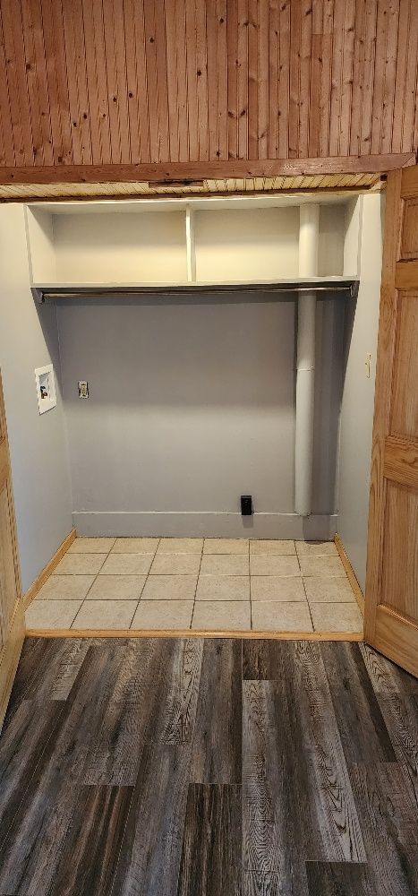 Closet with shelves, rod, and tiled floor, framed by wooden doors and wooden ceiling panels.