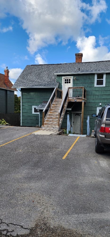 Green building with exterior stairs and parking lot on a sunny day.