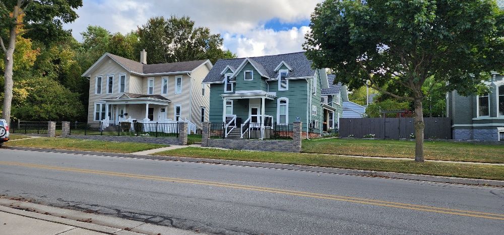 Row of houses along a street. The houses are light and teal with trees and a gray sky.