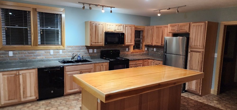 A kitchen with wooden cabinets, a black stove, a stainless steel refrigerator, and a wooden island.