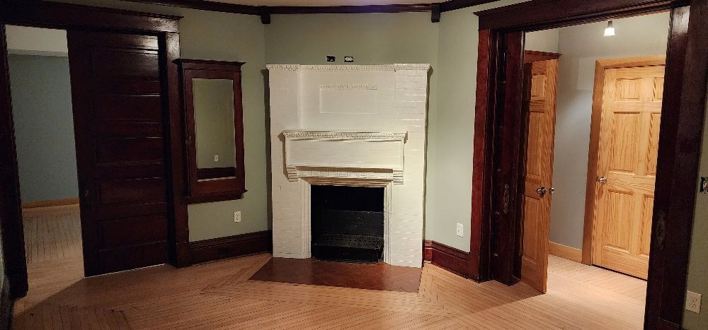 Room interior with fireplace, mirror, and dark wood trim. Light green walls, wooden doors, and light brown floor.