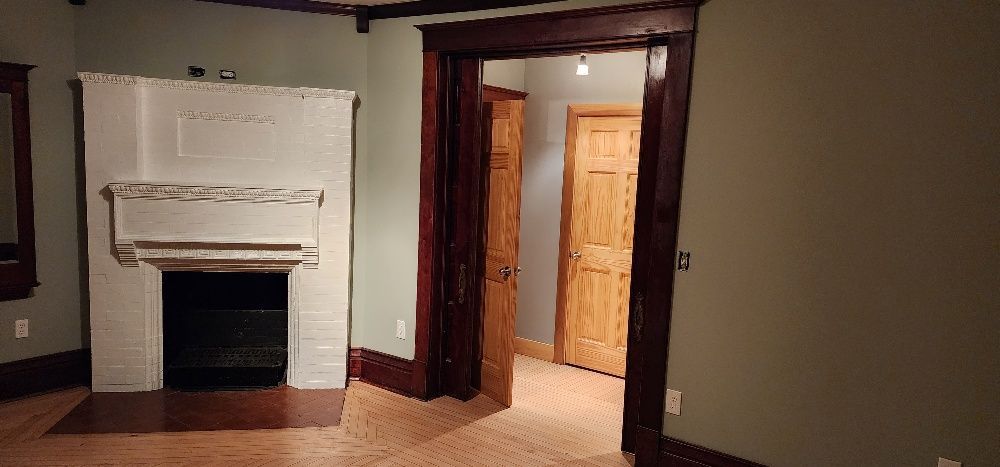 Room with fireplace and doorway, green walls, wooden trim and floors.