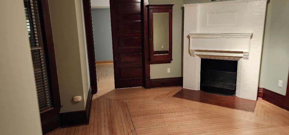 Room with a fireplace, hardwood floors, and a dark doorway. There is a mirror on the wall.