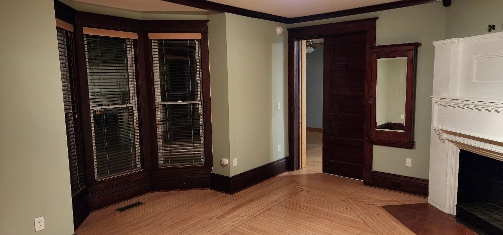 Room with bay windows, dark trim, green walls, wooden floor, sliding doors, and a fireplace.