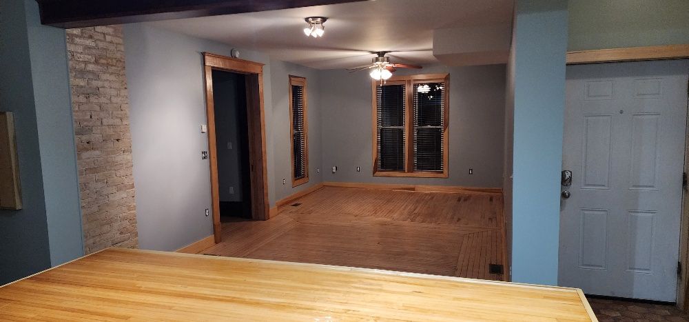 An empty room with wood floors and gray walls. A doorway leads to another room. A door on the right.