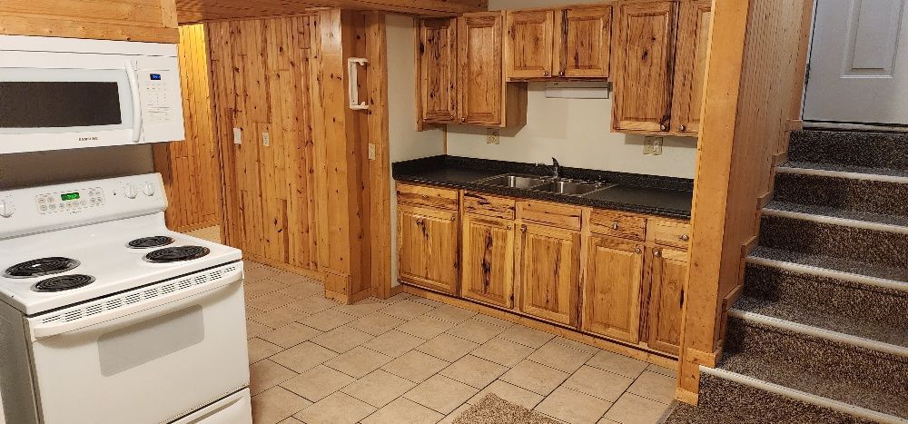 Kitchen with wooden cabinets, stove, microwave, and staircase.