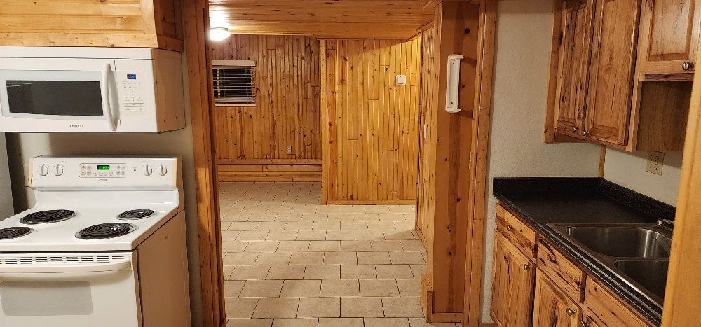 A kitchen with wood paneling, white appliances, a stove and microwave, and a black countertop.