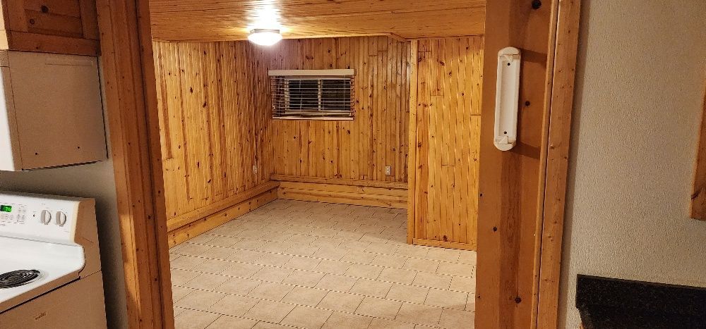 Wooden paneled room with light fixture. Open doorway framed by wood. White wall.