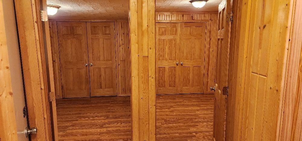 Wooden interior with multiple doors and light fixtures. The flooring and walls appear to be made of wood.