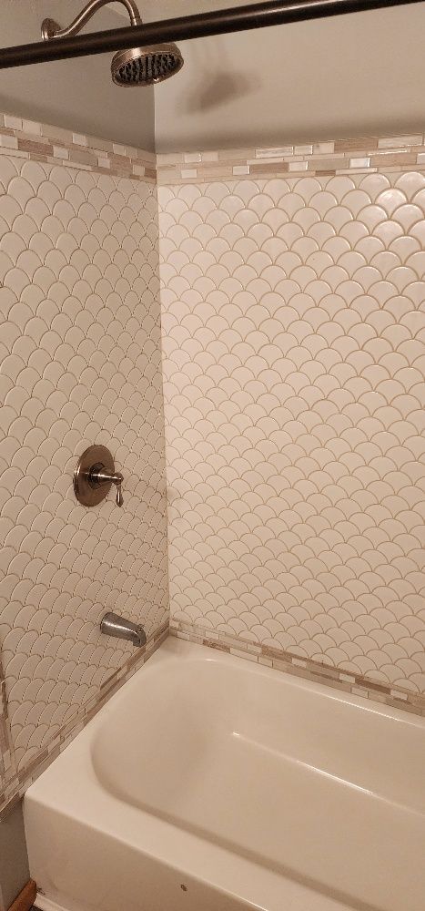 White tiled shower with a white bathtub. The shower head and faucet are visible.