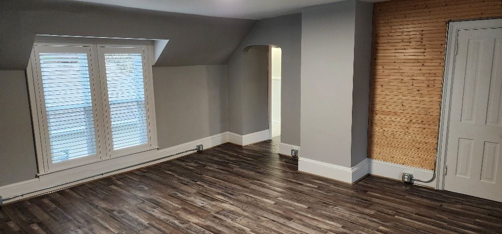 An empty room with dark wooden floor, gray walls, and a window with blinds.