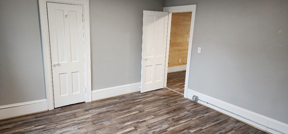 A room with gray walls and wood-look flooring. Two white doors are open.