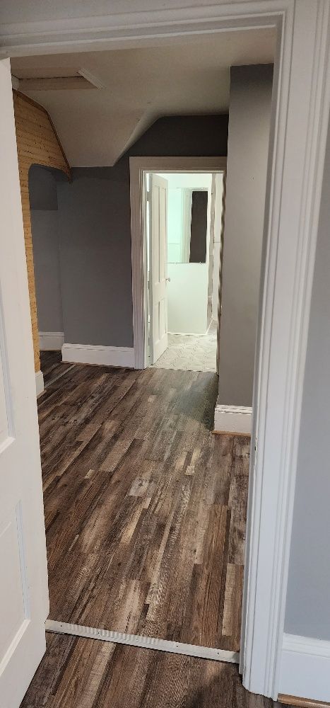 A hallway with wood-look flooring leads to an open doorway with a view of a bathroom.